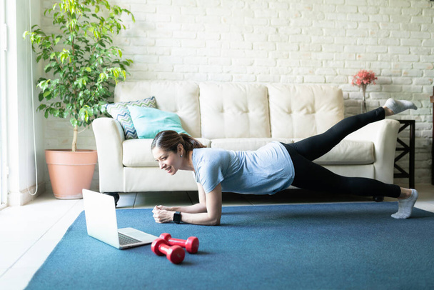 Ganzkörperansicht einer aktiven Frau in ihren Vierzigern nach einem Workout auf einem Laptop zu Hause - Foto, Bild