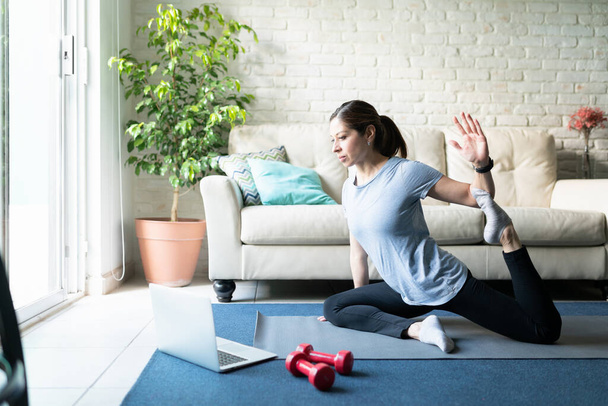40 'lı yaşlarda güzel, aktif bir kadının portresi çevrimiçi yoga rutinini takip ediyor ve evde egzersiz yapıyor. - Fotoğraf, Görsel