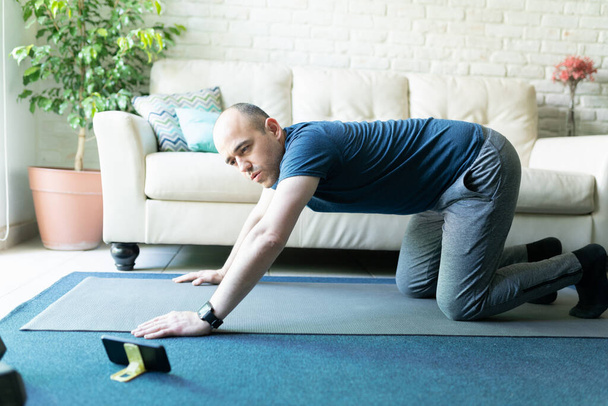 Caucasian man doing working out at home while following some exercises on his smartphone - Фото, изображение