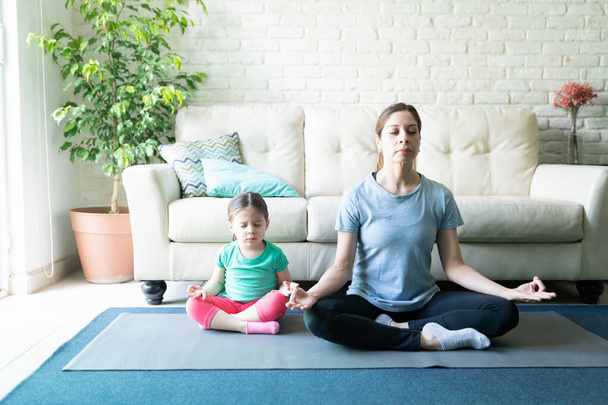 Pitkä näkymä äiti ja hänen tyttärensä harjoitellaan jooga ja meditointi yhdessä kotona
 - Valokuva, kuva