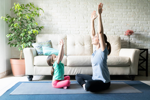 Linda niña tratando de imitar a su madre mientras practica yoga en casa y ambos se divierten
 - Foto, Imagen