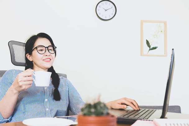 selective focus young beautiful asian woman smiling looking up, wore blue striped shirt Sitting at the desk,work online lifestyle relax at home with coffee ,home working with laptop,work from home - Fotografie, Obrázek