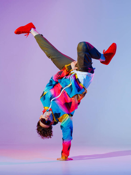 Guy dancing contemporary dance in studio. Neon light grey background. Acrobatic bboy dancer. Break dance lessons. - Photo, Image