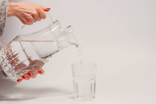 Drinking water. A female hand pours water from a decanter into a glass. - Foto, Bild
