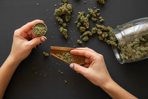 Close up of marijuana blunt with grinder. Woman preparing and rolling marijuana cannabis joint. Pot use concept. Close up Woman rolling a marijuana joint. - Photo, Image