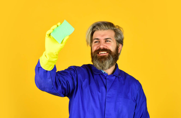 jarní úklid. pomocí houby na čištění. Manžel čistého domu. hygiena a čistota. vousatý muž nosí gumové rukavice. zralé školník v uniformě žluté pozadí - Fotografie, Obrázek