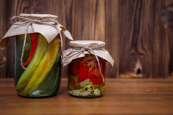 Pickled peppers in a jar on a wooden brown background, space for text. Homemade pickles. Canned vegetables.Preserves - Valokuva, kuva