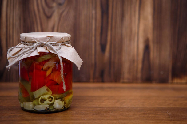 Sliced marinated peppers in a jar on a wooden brown background, space for text. Homemade pickles. - Foto, imagen