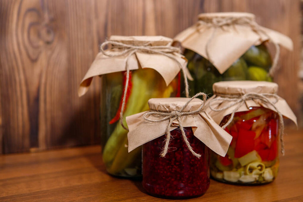 Preserved vegetables on wooden background.Homemade pickled cucumbers and peppers, and raspberry jam. - Fotó, kép
