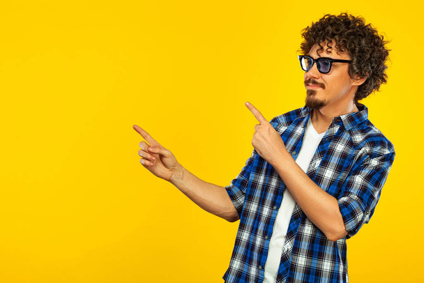 Closeup portrait of handsome happy european man with beard and curly hair in blue shirt opened mouth widely and shouting loud. Hispter isolated on yellow background. Positive emotions. - Foto, Bild