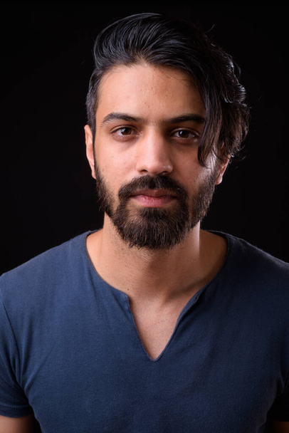 Studio shot of handsome bearded Persian man against black background - Photo, Image