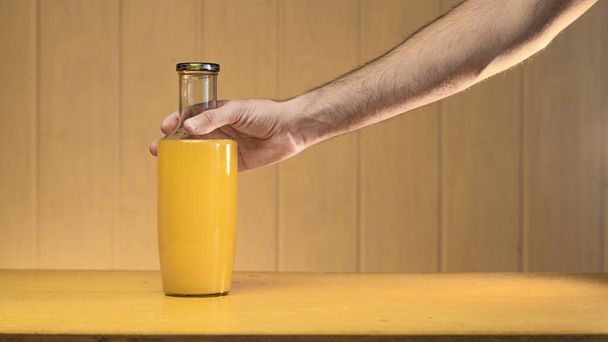 Een grote glazen fles met appelsap in de hand van een man op een houten achtergrond. - Foto, afbeelding