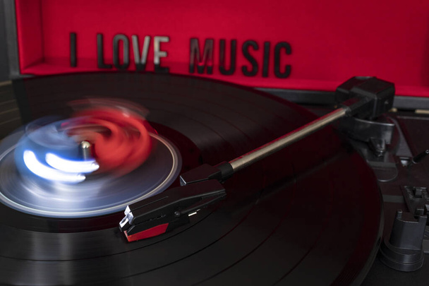 close up to a turn table needle playing a LP vinyl disc with turn table and I love music lettering over red background. music lovers concept. long exposure photography - Photo, Image