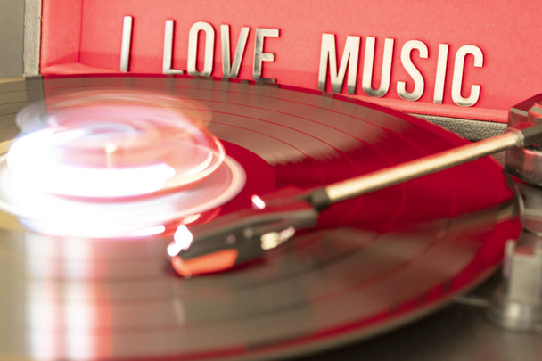 close up to a turn table needle playing a LP vinyl disc with turn table and I love music lettering over red background. music lovers concept. long exposure photography - Foto, afbeelding