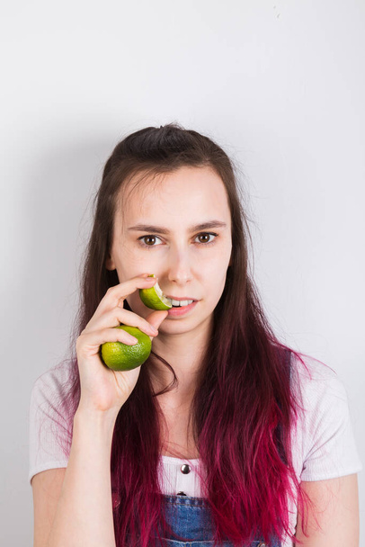 Young girl with pink hair eats lime on grey background - Zdjęcie, obraz