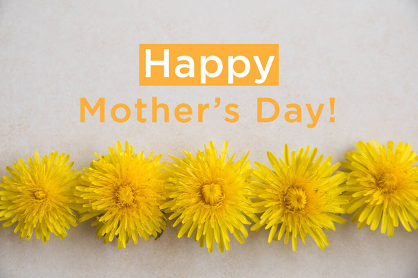 Happy Mothers Day. Gelber Löwenzahn liegt auf einer leicht strukturierten Oberfläche. Hochzeitskarte. Flache Lage, Draufsicht - Foto, Bild
