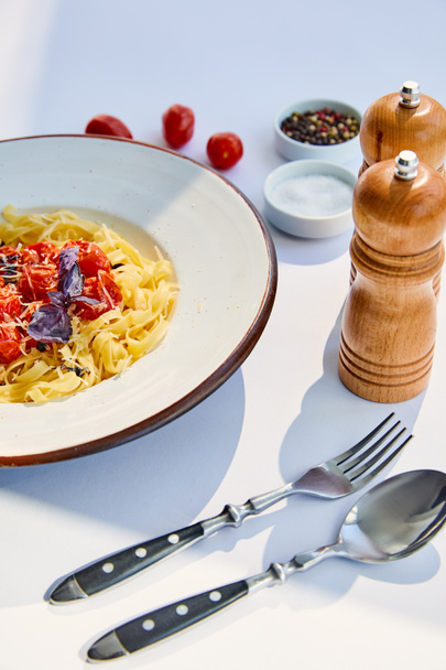 deliciosa pasta con tomates servida con cubiertos, molinos de sal y pimienta en mesa blanca a la luz del sol
 - Foto, Imagen