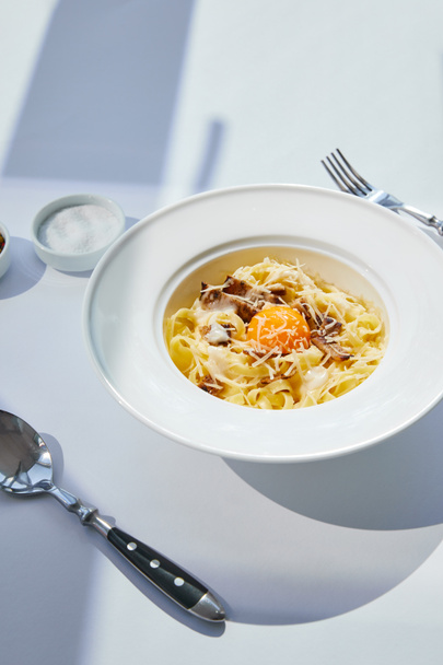 delicious pasta carbonara served with cutlery and salt on white table in sunlight - Foto, Imagem