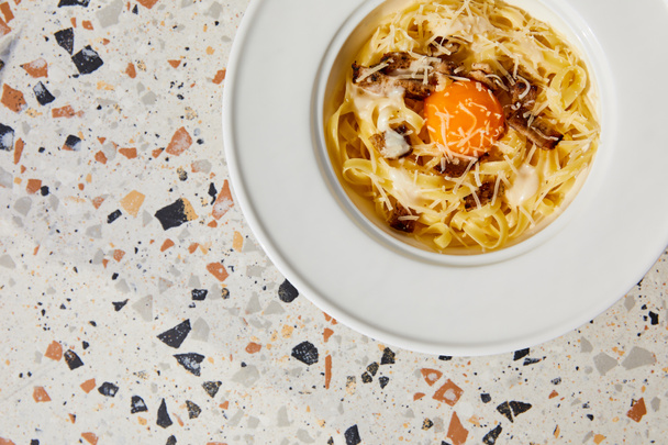 bovenaanzicht van heerlijke pasta carbonara geserveerd in ronde plaat op stenen tafel - Foto, afbeelding