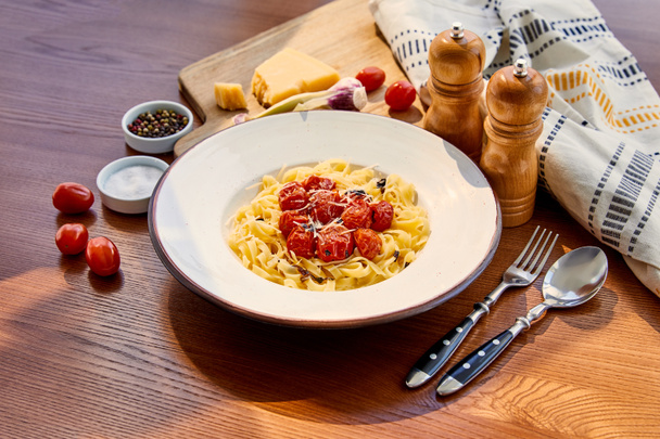 delicious pasta with tomatoes served on wooden table with cutlery, napkin, seasoning and ingredients in sunlight - Foto, imagen