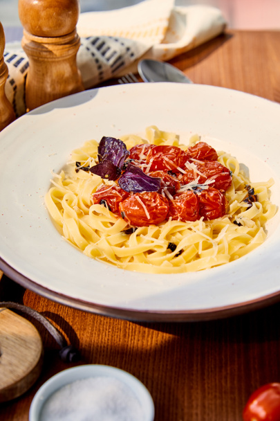 delicious pasta with tomatoes, parmesan and red basil served on wooden table in sunlight - Fotó, kép