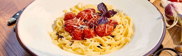 delicious pasta with tomatoes, parmesan and red basil served on wooden table in sunlight, panoramic shot - 写真・画像