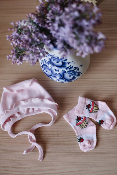 Beautiful pink baby clothes. Home cosiness. baby booties and clothes with a bouquet of flowers on the background. Newborn clothes - Φωτογραφία, εικόνα