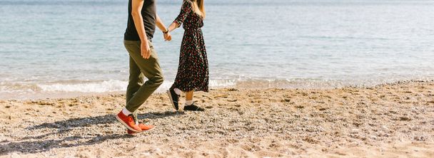 ragazzo e ragazza stanno camminando lungo la spiaggia soleggiata tenendosi per mano - Foto, immagini