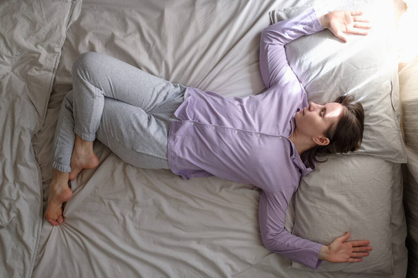 Молодая белая женщина, тренирующаяся дома на кровати, делает спинальный твист в вариации гарудасаны, отдыхает после утренней тренировки
 - Фото, изображение