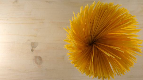 Сверху вниз плоский вид на горстку спагетти спицы пятна, которые выглядят как желтый цветок на светлом деревянном столе фон итальянской кухни кухня копировать пространство
 - Фото, изображение