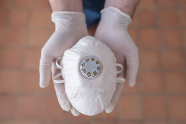 Sluit de handen met een medisch gezichtsmasker voor bescherming. Twee handen met witte veresterde handschoenen met een medisch masker. Bescherming tegen CORONAVIRUS, ziekten, infecties en virussen. COVID-2019 - Foto, afbeelding