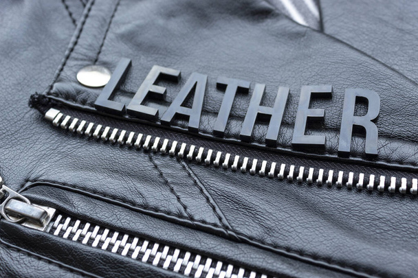 Closeup to a LEATHER lettering word over a black leather biker jacket. Fashion, clothes lifestyle and concept photography - Photo, Image