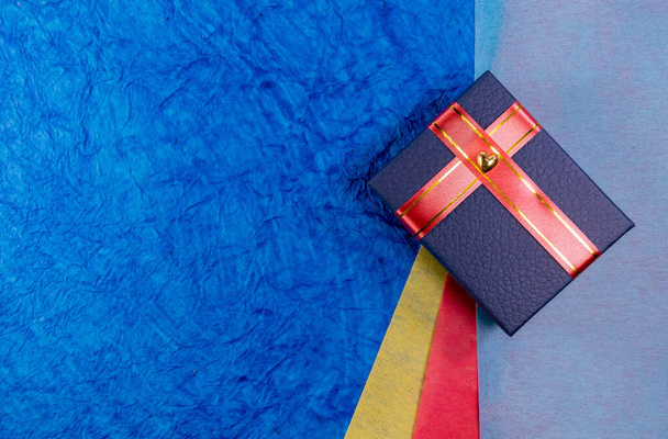 Верхний снимок голубой подарочной коробки с сердцем и красными лентами поверх цветных бумаг на заднем плане. Подарок для девочек
 - Фото, изображение