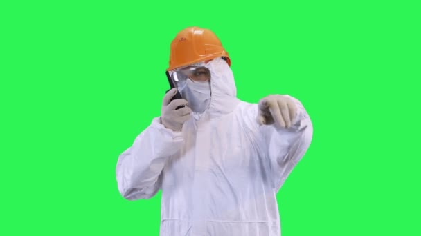 A man in a helmet and protective suit speaks on the radio in elevated tones.Green screen background. - Video