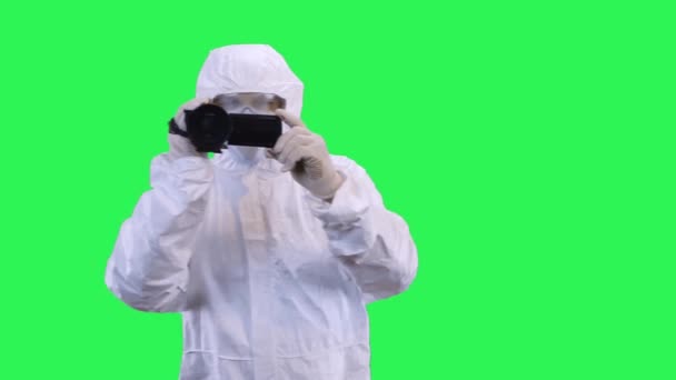 A man in a protective suit and goggles is filming a video camera with his hands.Green screen background. - Video