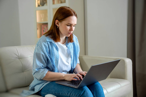 Frau benutzt Laptop, tippt Text, sitzt auf Sofa. - Foto, Bild