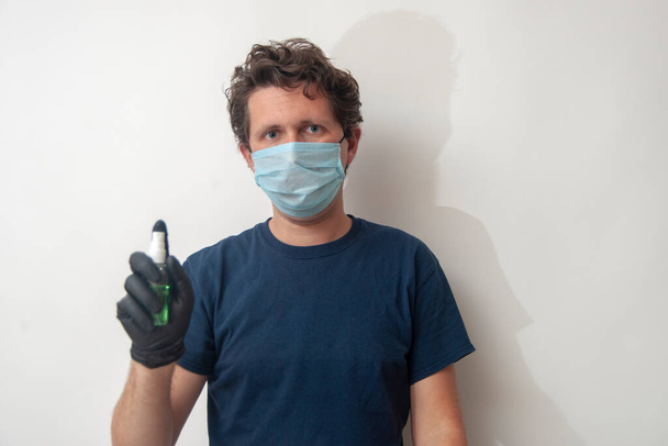 El joven lleva una máscara médica azul y guantes negros con desinfectante.
. - Foto, Imagen