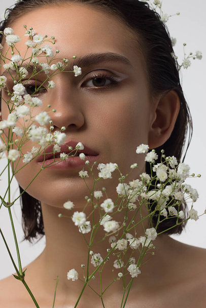 Close up portrait of a face with beautiful skin and nude makeup, eyeliner and long eyelashes, puffy natural lips and white flowers. Fashion photography. Cosmetology and spa. Freshness of spring - Fotoğraf, Görsel