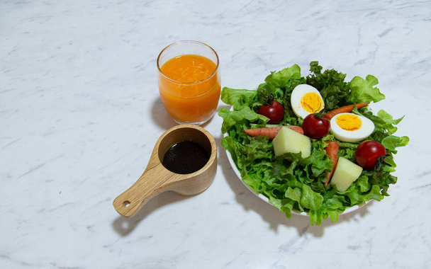 Νόστιμο φρέσκο μείγμα λαχανικών σαλάτα σε λευκό πιάτο με χυμό πορτοκαλιού σε λευκό μάρμαρο φόντο Πράσινο φυτικό καρότο ντομάτας και μείγμα αυγών με βαλσάμικο βινεγκρέτ είναι υγιεινό φαγητό - Φωτογραφία, εικόνα