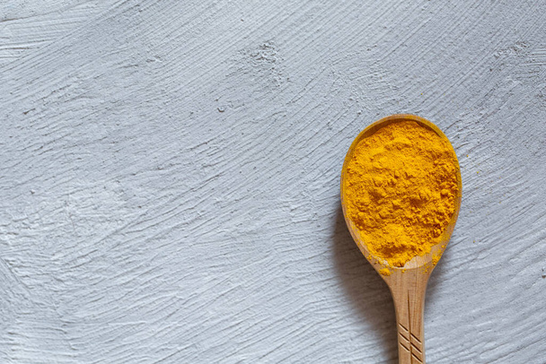 Natural medicine for immunity. Indian turmeric spice in a wooden spoon on a gray background.  - Фото, изображение