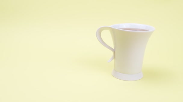 Hohe weiße Tasse Tee auf gelbem Hintergrund. - Filmmaterial, Video