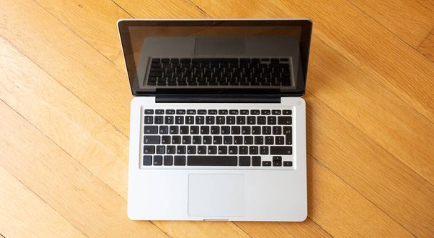 Laptop offen auf Holzboden, Arbeiten von zu Hause aus, Blick von oben - Foto, Bild