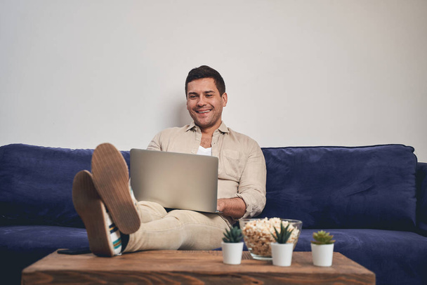 Smiling man with a laptop on his knees - 写真・画像