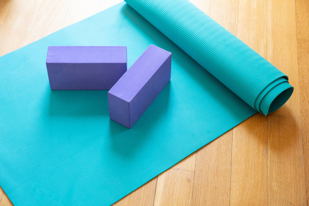 Yoga mat en oefenstenen op houten vloer. Pilates, yogales, thuis trainen en een gezond levensstijl concept - Foto, afbeelding