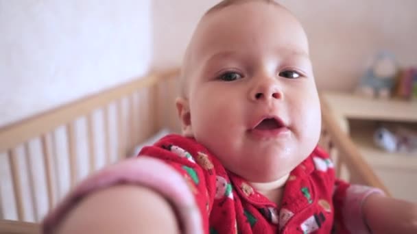Funny Baby Stands In Bed And Looks At Camera. Child Stretches Hands Into Camera. The kid in the children's room is in the crib. The child reaches for the camera and looks into it. - Materiał filmowy, wideo