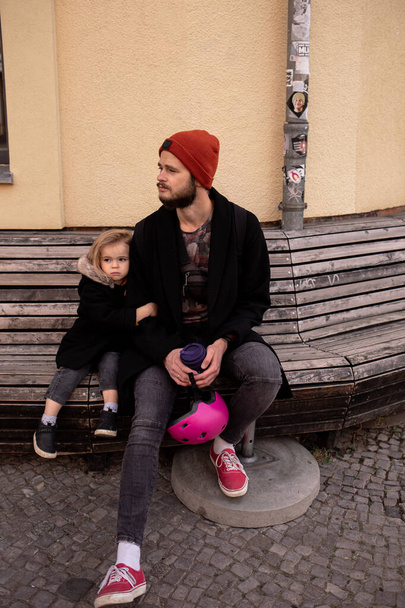 Linda niña con papá sentado en un banco en una calle vacía, extrañando a sus amigos
  - Foto, Imagen
