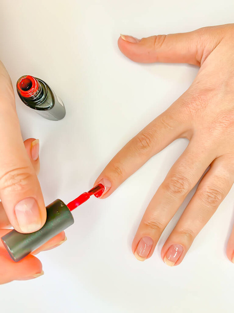 Zamknij się kobieta malowanie paznokci z lakierem do paznokci w kolorze czerwonym na białym tle. Samodzielny manicure w domu - Zdjęcie, obraz