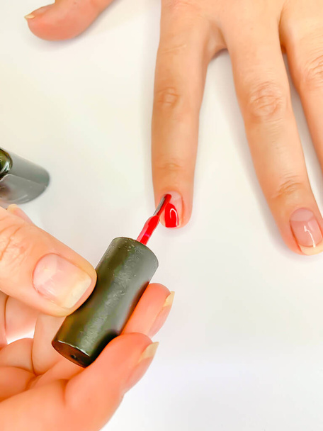 Gros plan femme peignant ses ongles avec du vernis à ongles de couleur rouge sur fond blanc. Auto manucure à la maison
 - Photo, image
