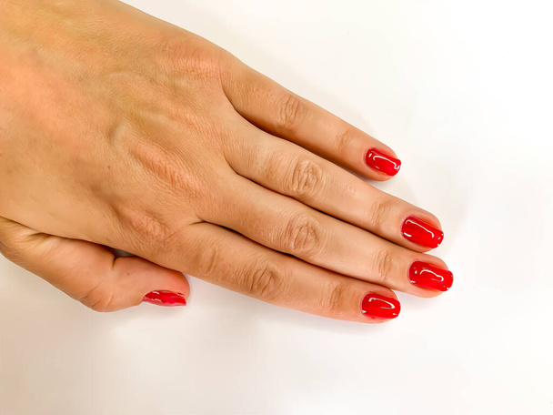 Cerca de la mano de la mujer con las uñas rojas sobre un fondo blanco. Auto manicura en casa
 - Foto, Imagen