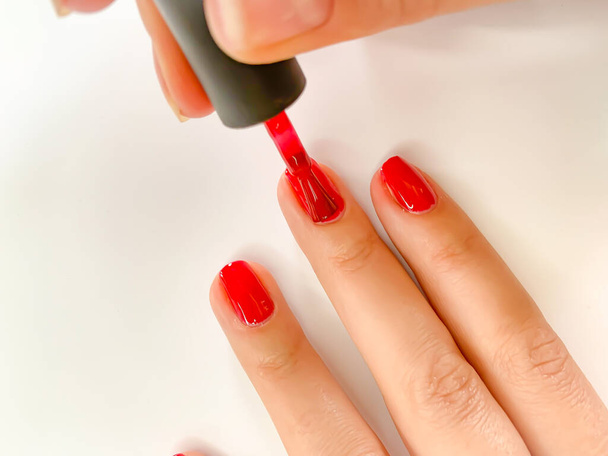 Close-up weibliche Frau lackiert ihre Nägel mit Nagellack in roter Farbe auf weißem Hintergrund. Selbstmaniküre zu Hause - Foto, Bild